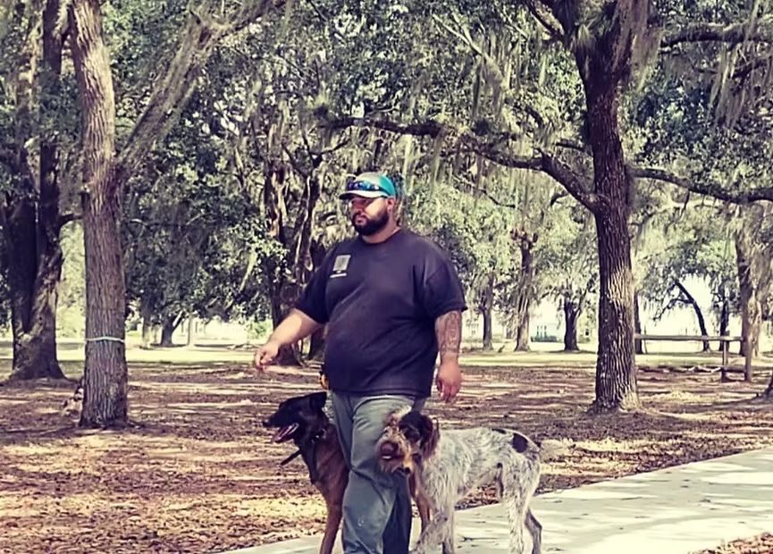 Zac Thomas walking two dogs at heel under the live oaks