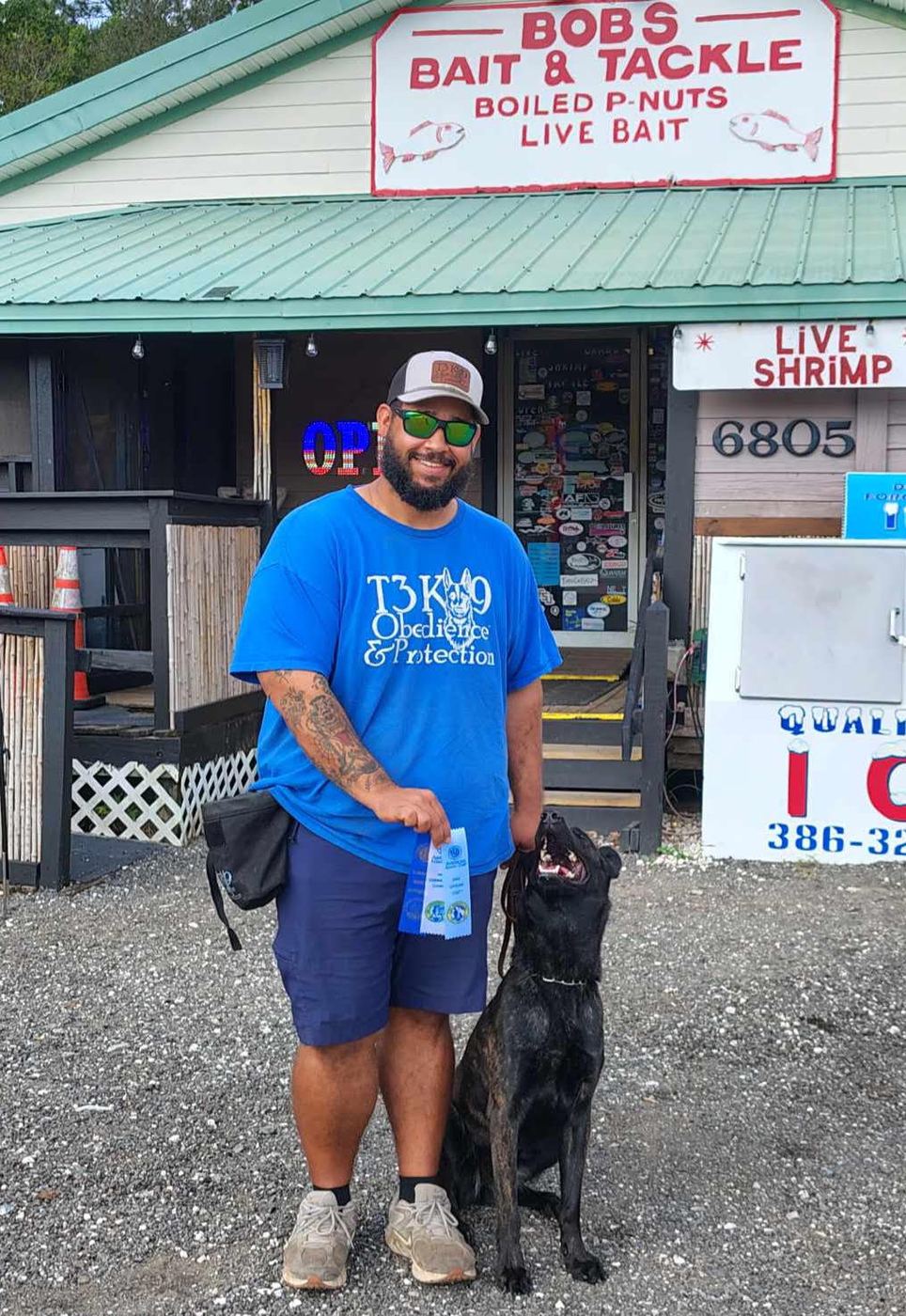 Zac Thomas holding ribbons with a brindle Dutch Shepherd sitting at his side and looking up at him